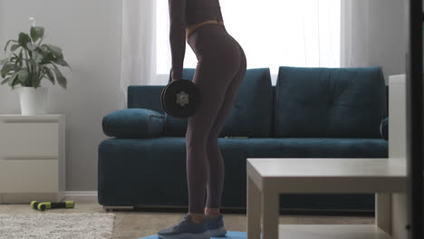 young-sporty-woman-with-dumbbells-is-leaning-forward-in-living-room-fitness-at-home-healthy-lifestyle-and-wellness-power-training
